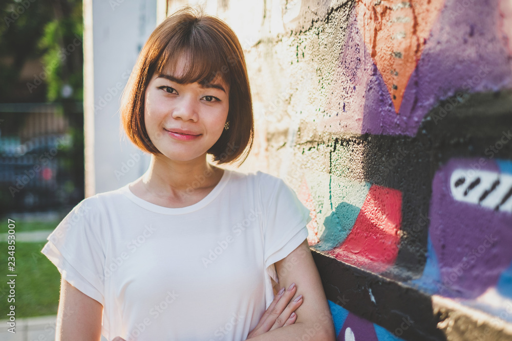 Fototapeta premium Beautiful asian woman looking at the camera while standing on a Street Art Graffiti wall background