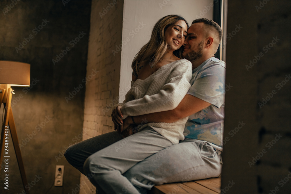 A young couple in love is hugging and smiling next to the window. A young couple in love is hugging and smiling next to the window.