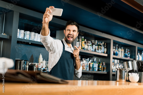 Barman standing with smartphone and taking selfie in bar