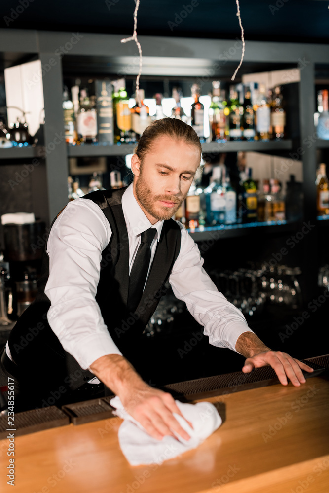 Handsome barman cleaning wooden bar counter with white napkin Handsome barman cleaning wooden bar counter with white napkin