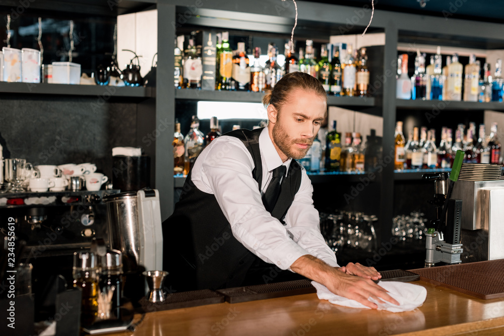 Bartender cleaning wooden bar counter with white napkin