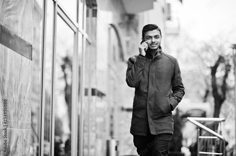 Stylish indian hindu man in gray coat posed on street and speaking at phone.