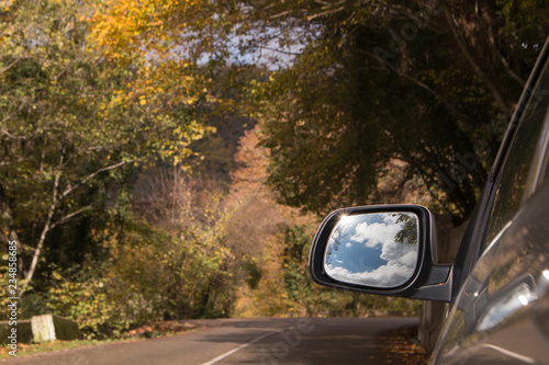 Travel concept. Beautiful sky and clouds in sideview car mirror on mountain road