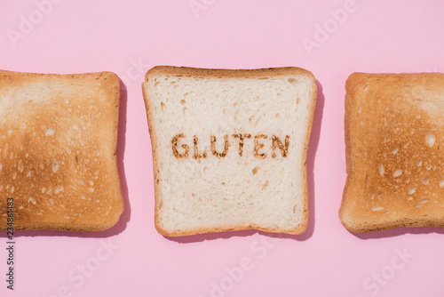 top view of row of toasts and slice of bread with burned gluten sign on pink surface