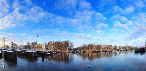 Beautiful 180 degree cityscape panorama of the river Amstel in Amsterdam, the Netherlands, in winter with ice and snow with the famous skinny bridge (magere brug)