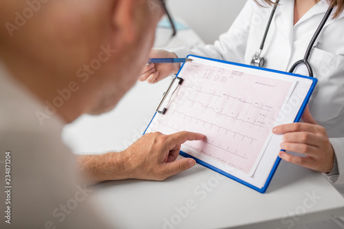 medicine, age, health care, cardiology and people concept - close up of senior man and doctor with cardiogram on clipboard at hospital photo
