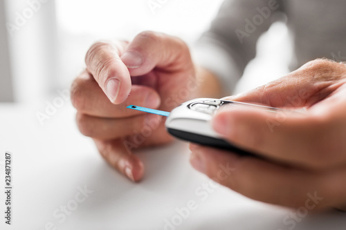 medicine, age, diabetes, health care and old people concept - senior man with glucometer checking blood sugar level at home
