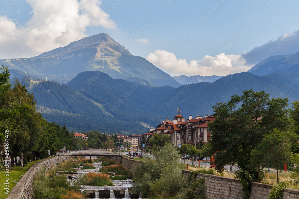 View of Bansko town, bulgarian ski resort in summer, Pirin Mountains in the background, a river in the foreground, Bulgaria.