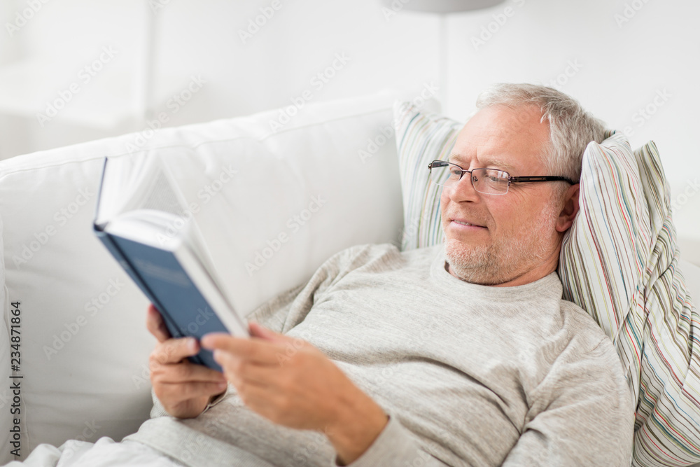 old age, leisure and people concept - senior man lying on sofa and reading book at home old age, leisure and people concept - senior man lying on sofa and reading book at home