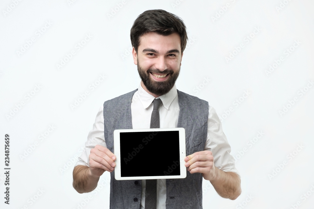 Cheerful young hsipanic man holding tablet with blank screen over grey background Cheerful young hsipanic man holding tablet with blank screen over grey background
