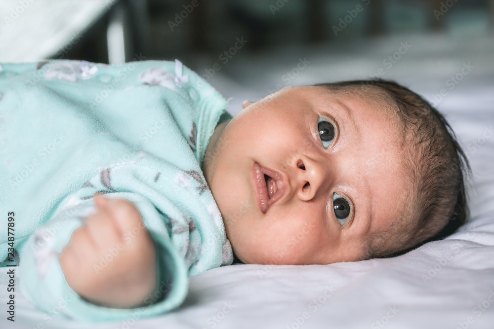 Baby with brown eyes closeup lying on the bed in blue clothes Baby with brown eyes closeup lying on the bed in blue clothes