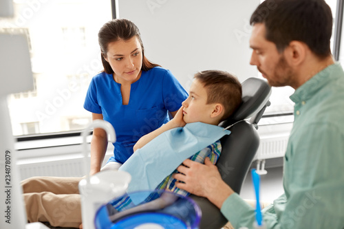 medicine, dentistry and healthcare concept - father and son suffering from toothache visiting dentist at dental clinic