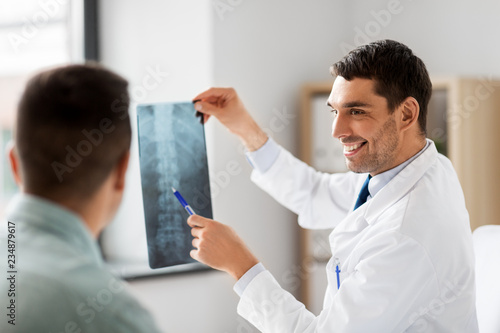 medicine, healthcare and people concept - smiling doctor showing x-ray to patient at medical office in hospital photo