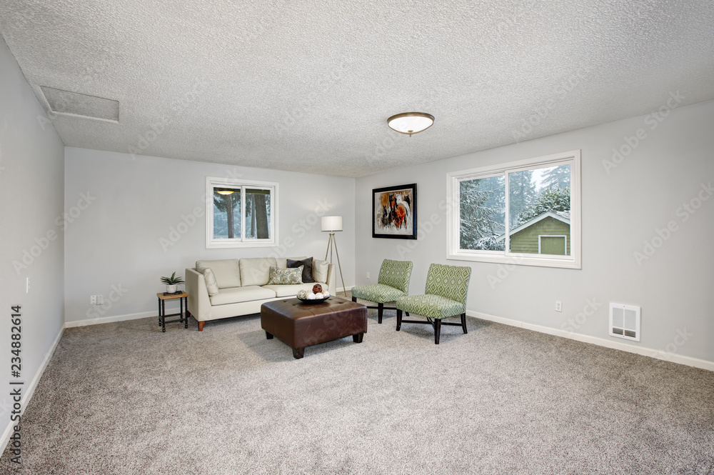 Fototapeta premium Light grey living area with green chairs and leather ottoman