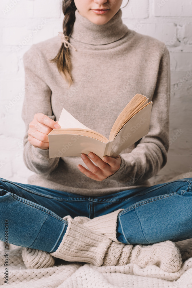 Obraz premium cropped shot of girl in knitted socks sitting and reading book