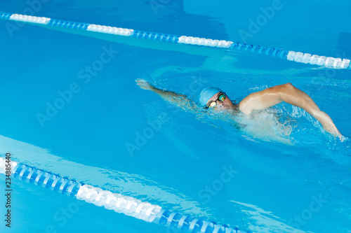 Photo of sports man in blue cap swimming in pool