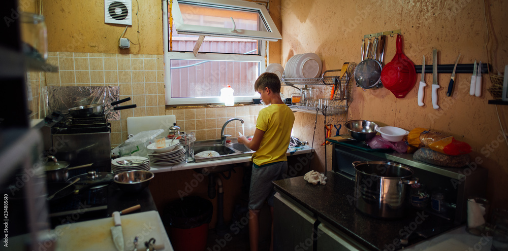 boy washing dishes in the kitchen in yellow t-shirt
