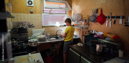 Fotografie boy washing dishes in the kitchen in yellow t-shirt