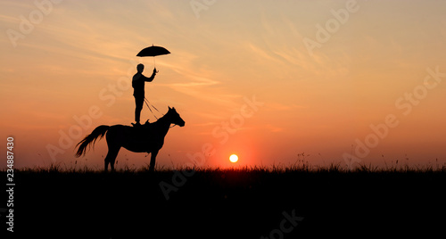 Horsemanship and trick-riding scene: men, standing on horse with open umbrella. Romantic scene on idyllic sunset. 