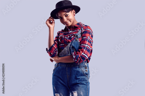 Elegant black hipster girl with short hair in a plaid shirt and denim overalls. © micro