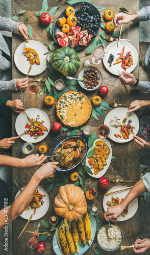 Thanksgiving, Friendsgiving holiday celebration. Flat-lay of friends feasting at Thanksgiving Day table with turkey, pumpkin pie, roasted vegetables, fruit, rose wine, top view, vertical composition