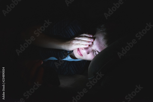 Depressed teenager lying on a couch in the dark while on his cell phone.