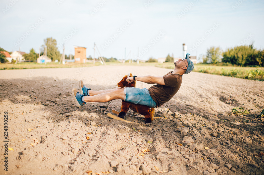 Φωτογραφία Adult stylish man riding wooden toy horse on field outdoor
