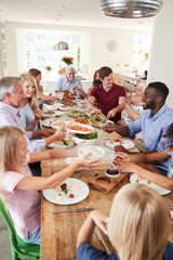 Group Of Multi-Generation Family And Friends Sitting Around Table And Enjoying Meal