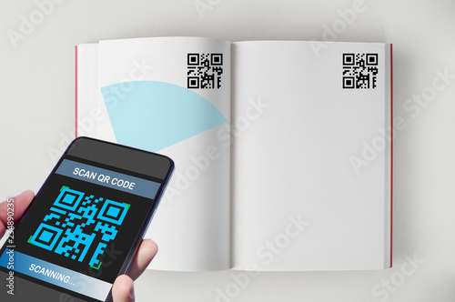 Hand holding smartphone with scanning QR code on open book screen on white background, smart technology concept and QR codes link the book to the internet idea