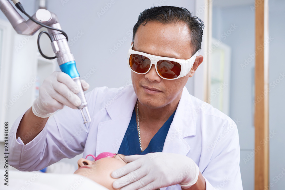 Male beautician wearing special glasses when using laser to remove facial hair of female client Male beautician wearing special glasses when using laser to remove facial hair of female client