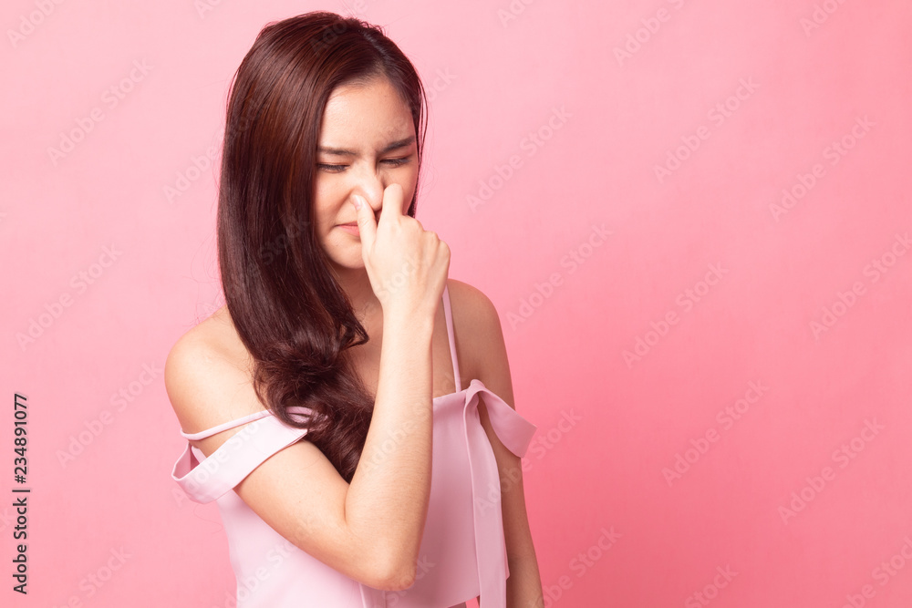 Young Asian woman holding her nose because of a bad smell on pink background Young Asian woman holding her nose because of a bad smell on pink background