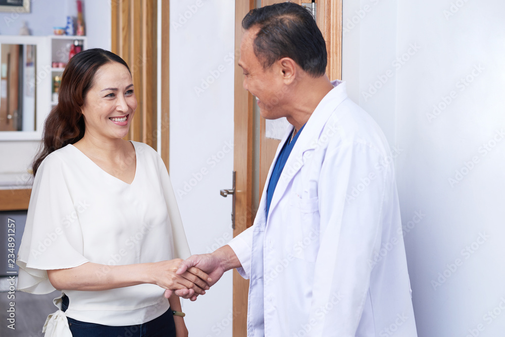 Pretty smiling mature Vietnamese woman shaking hand of her plastic surgeon Pretty smiling mature Vietnamese woman shaking hand of her plastic surgeon