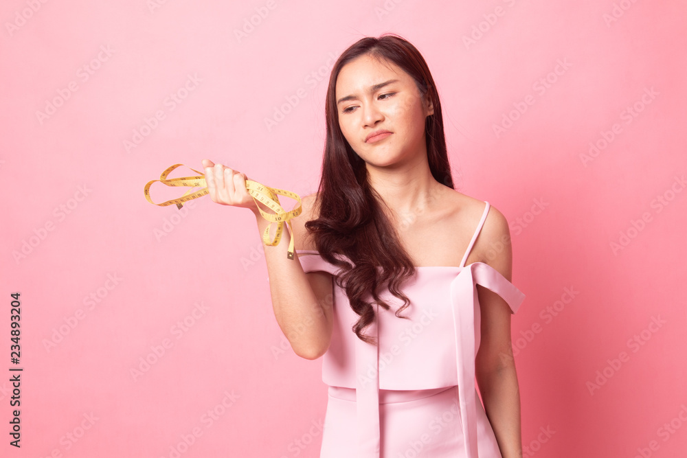 young Asian woman unhappy with her diet holding measuring tape on pink background young Asian woman unhappy with her diet holding measuring tape on pink background