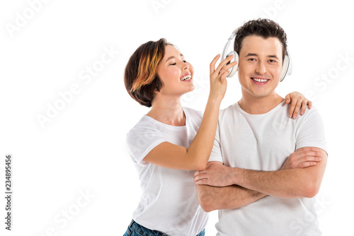 happy wife putting headphones on smiling husband isolated on white