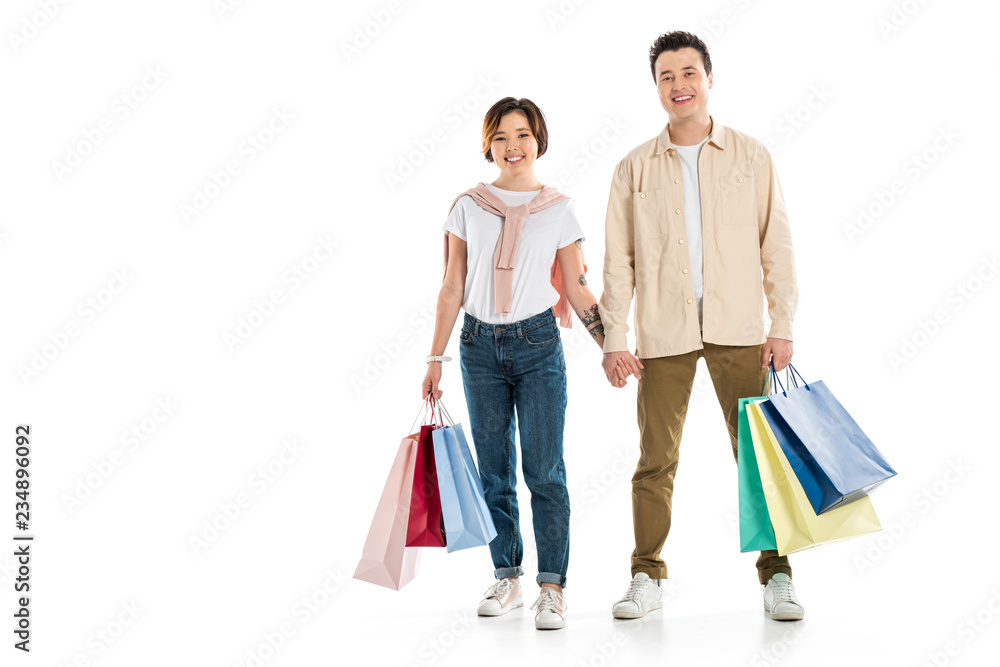 smiling couple looking at camera, holding hands and carrying shopping bags isolated on white smiling couple looking at camera, holding hands and carrying shopping bags isolated on white