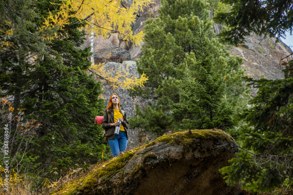 Profile view of young long-haired barefooted tourist girl sitting on huge rock with enjoying fantastic view of mountains covered with pine forest.