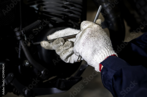 Image is Close up,People are repairing a motorcycle Use a wrench and a screwdriver to work. © Suppasit