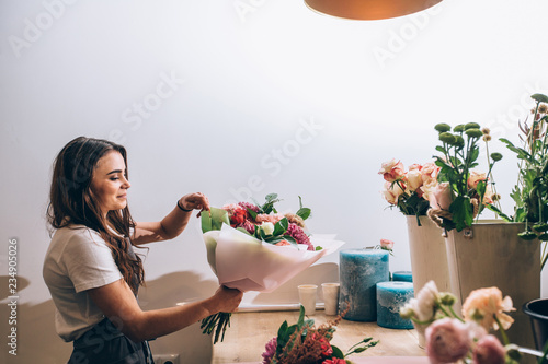 Foto Young smiling brunette female business woman florist creating beautiful bouquet of colorful different flowers in modern interior floral shop