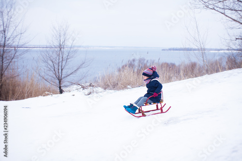 Little girl sliding sown the hill on sledge with snow around