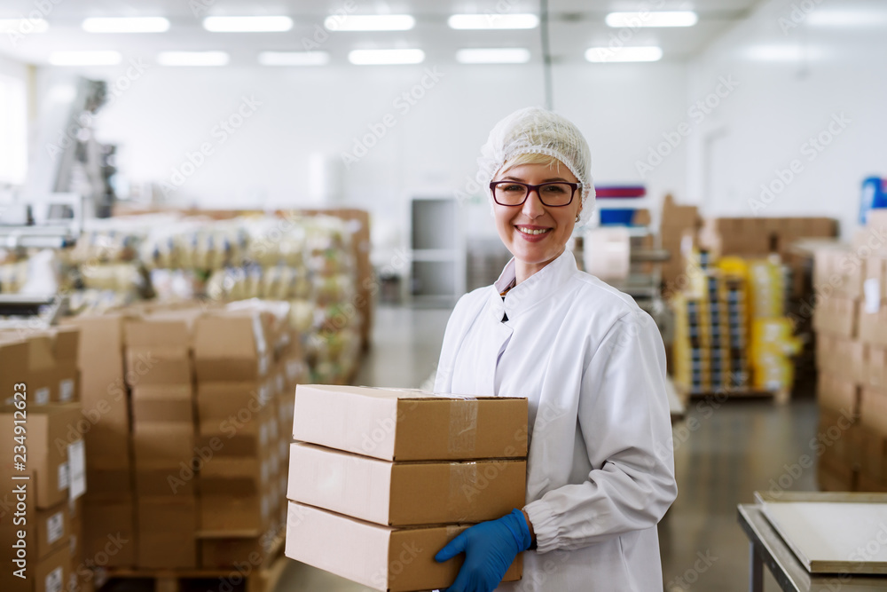 Happy Caucasian female worker holding boxes while standing in warehouse. Happy Caucasian female worker holding boxes while standing in warehouse.