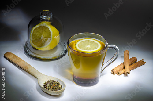 Herb tea in white cup with ginger, lemon slices, cinnamon sticks, honey, white wood background
