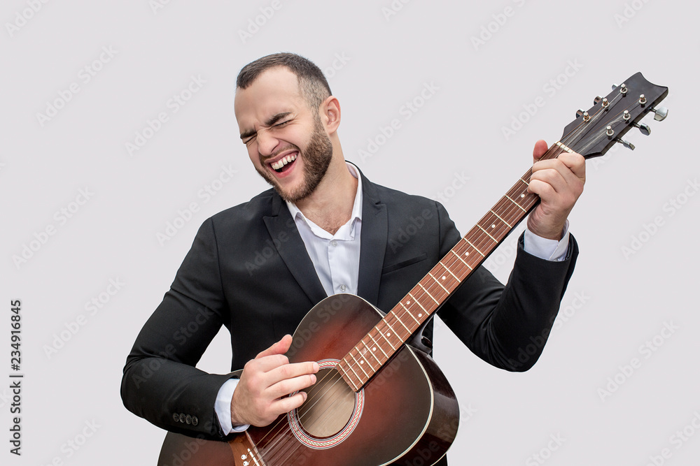 Singer in black suit stand and play on guitar. He sing song. Young man wears suit. Isolated on white background.
