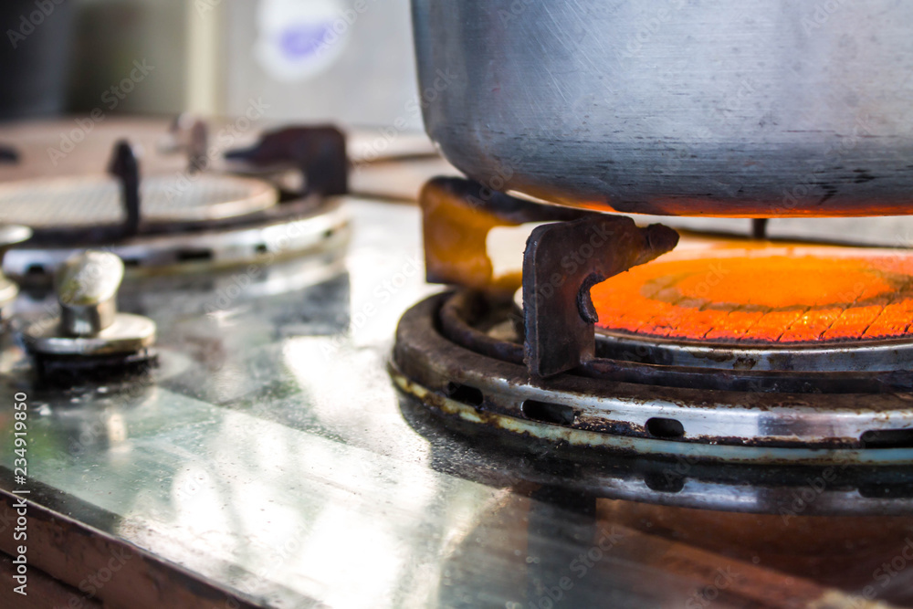 Fototapeta premium Old gas stove with stainless steel container. There is a half orange flame.