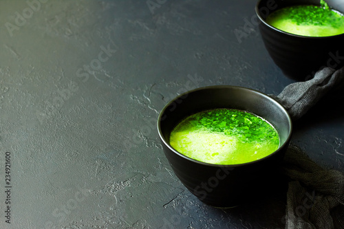 Fresh homemade spinach cream soup in dark bowls on dark concrete background with copy space