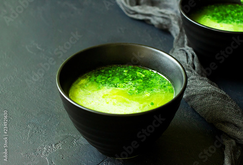 Fresh homemade spinach cream soup in dark bowls on dark concrete background with copy space