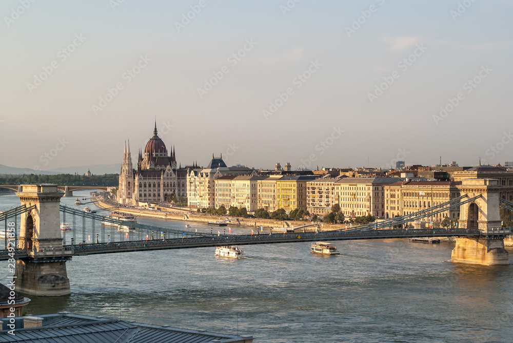 Panoramic view from the Castle hill in Budapest during sunset of the Hungarian Parliament building, the Chain Bridge of the Danube with cruise ships and the buildings on the river bank. 