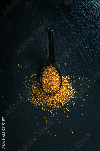 Golden beads in spoon on black background. christmas decorations flat lay