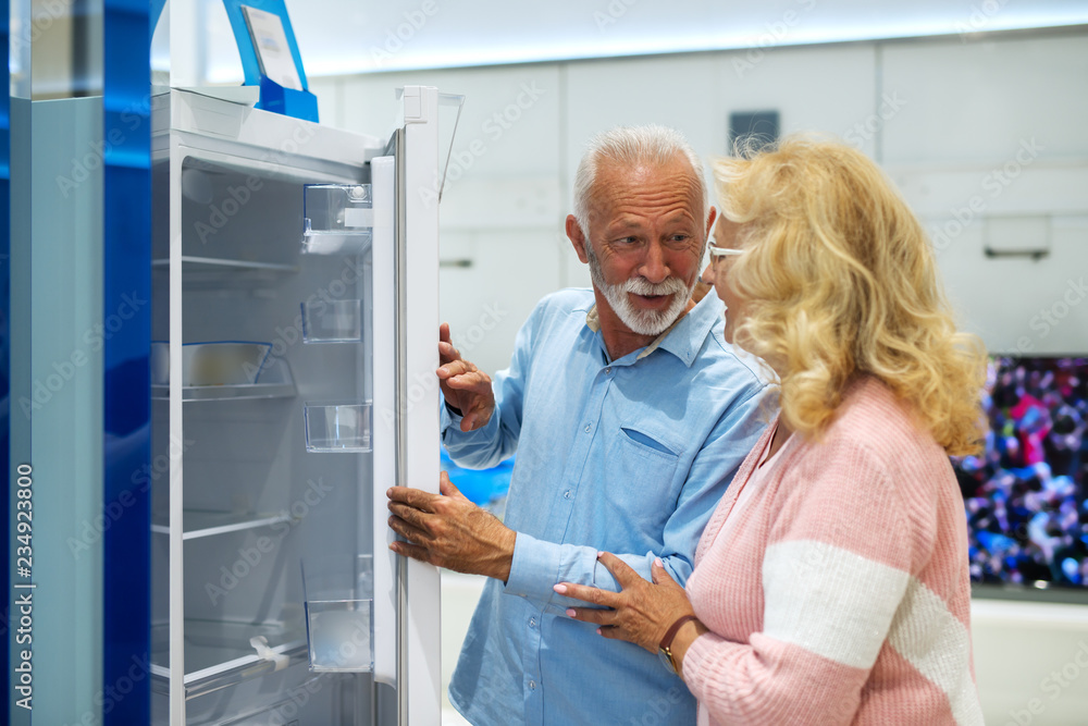 Caucasian senior couple buying new fridge. Tech store interior. Caucasian senior couple buying new fridge. Tech store interior.
