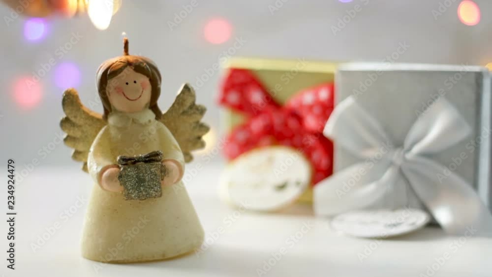 Hand lights an angel candle. Christmas atmosphere with gift boxes and christmas lights on the background Hand lights an angel candle. Christmas atmosphere with gift boxes and christmas lights on the background