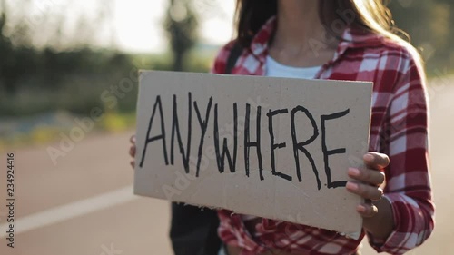 Young beautiful woman hitchhiking standing on the road holding anywhere sign. Summer time